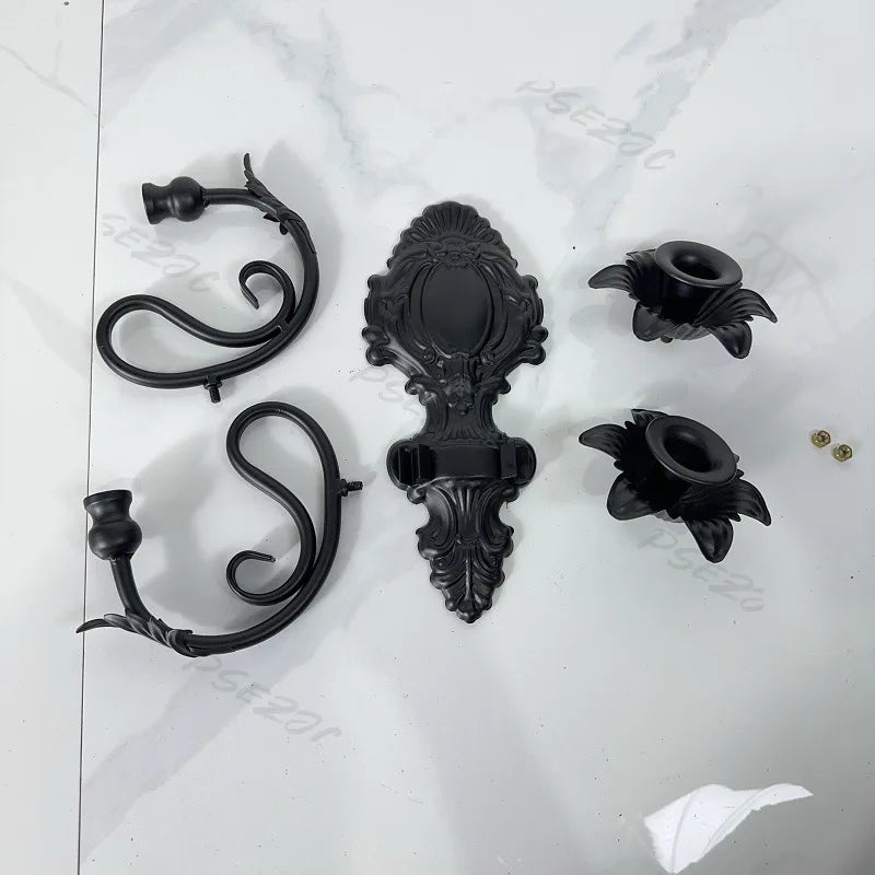 Éléments d’une applique murale décorative noire présentés démontés, avec bras, support central et porte-bougies.
