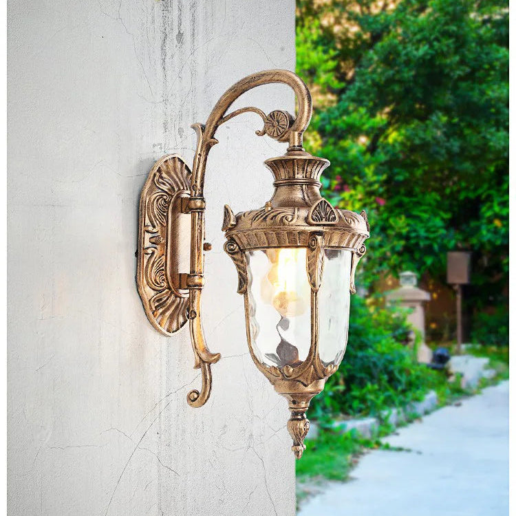 Applique murale extérieure vintage en métal bronze installée sur un mur avec jardin en arrière-plan