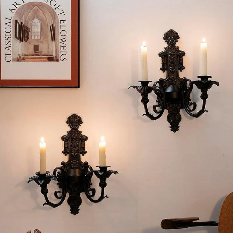 Deux appliques murales décoratives noires avec bougies allumées fixées sur un mur clair.