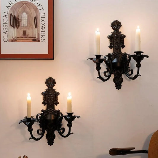 Deux appliques murales décoratives noires avec bougies allumées fixées sur un mur clair.