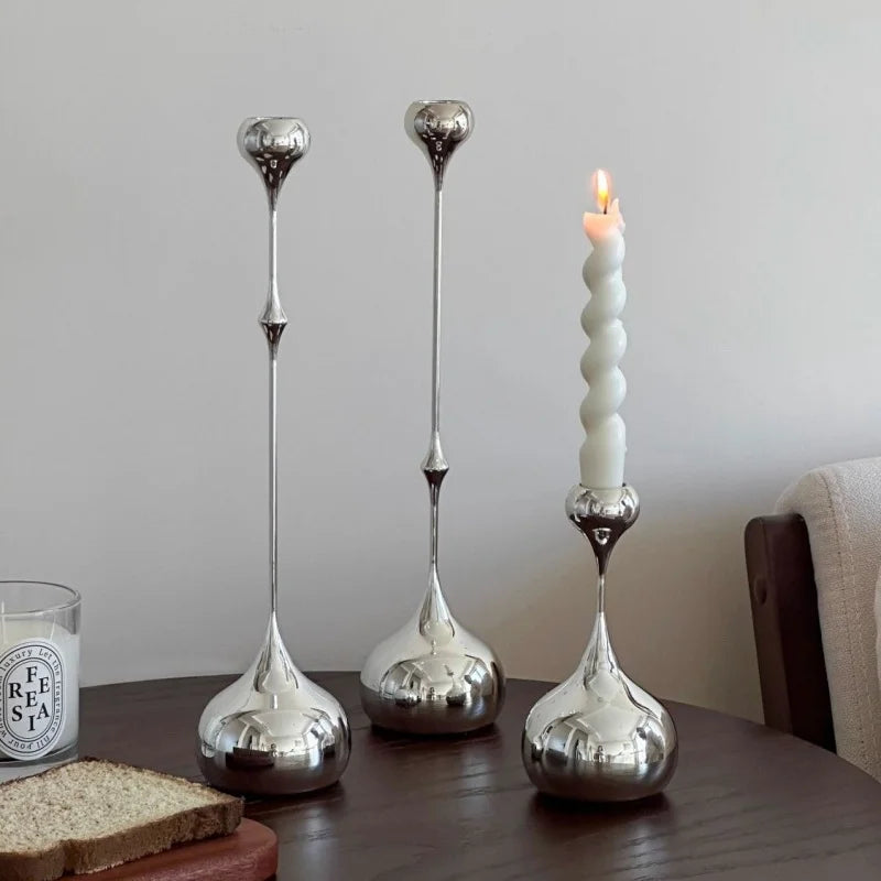 Bougeoir décoratif en métal argenté tenant une bougie allumée sur une table.