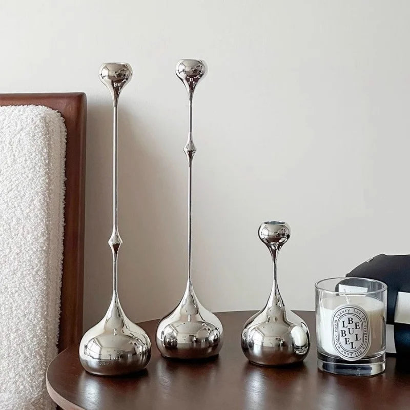 Trois bougeoirs décoratifs en métal argenté posés sur une table avec une bougie.