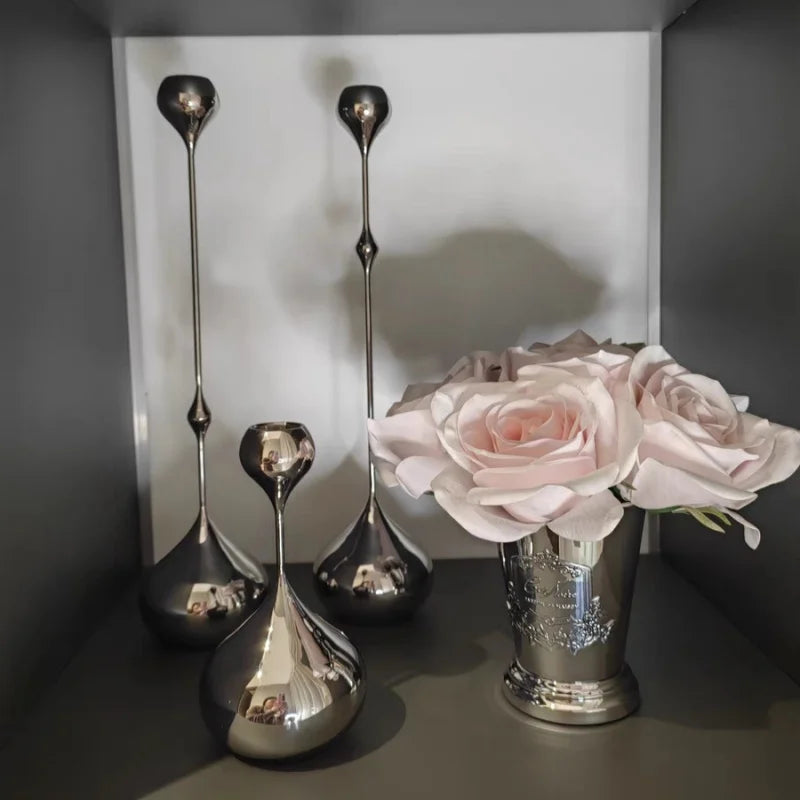Bougeoirs décoratifs en métal argenté présentés sur une étagère avec un vase de fleurs.