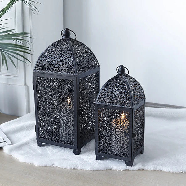 Deux lanternes décoratives noires en métal ajouré posées en intérieur avec bougies allumées.