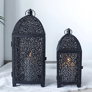 Lanternes décoratives noires ajourées disposées en intérieur avec bougies allumées.