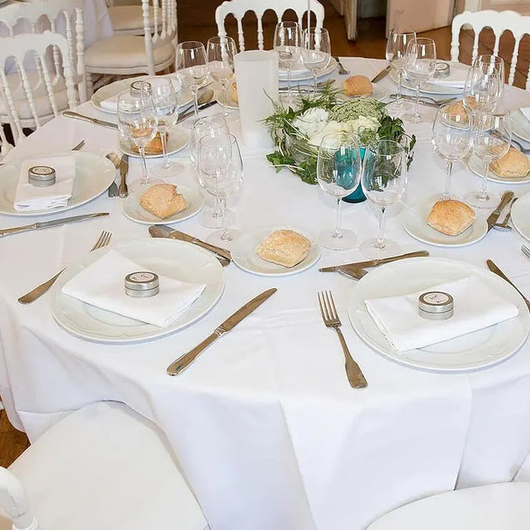 Nappe ronde blanche sur table dressée pour repas formel ou réception.