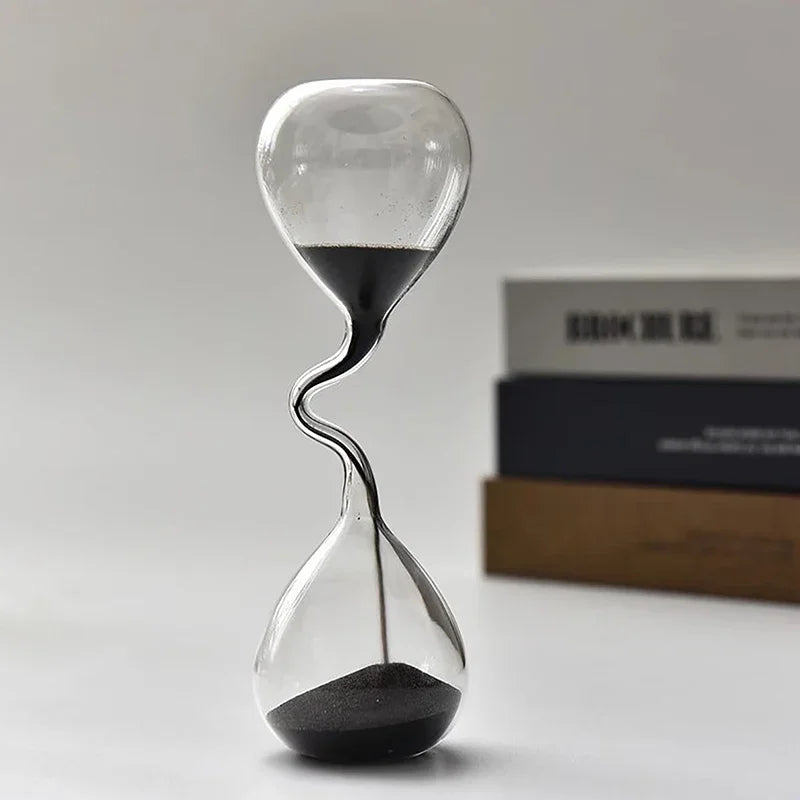 Sablier décoratif en verre avec sable noir, présenté debout sur une surface claire.