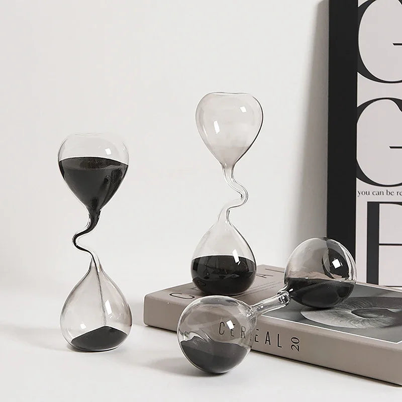 Ensemble de sabliers décoratifs en verre avec sable noir, disposés sur une table.