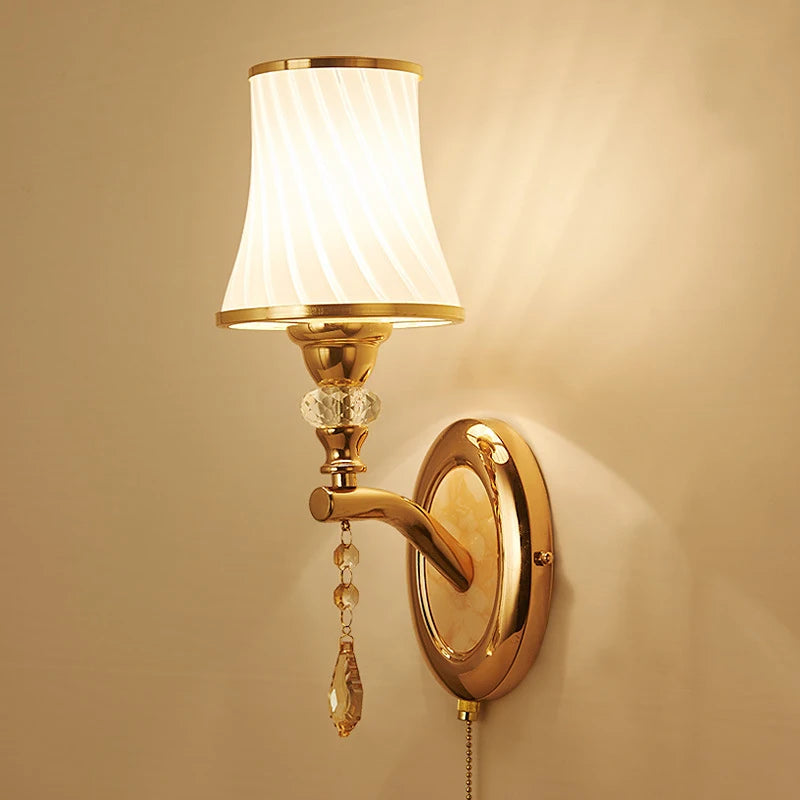 Applique murale dorée allumée diffusant une lumière chaude et dorée, finition métal doré et verre plissé