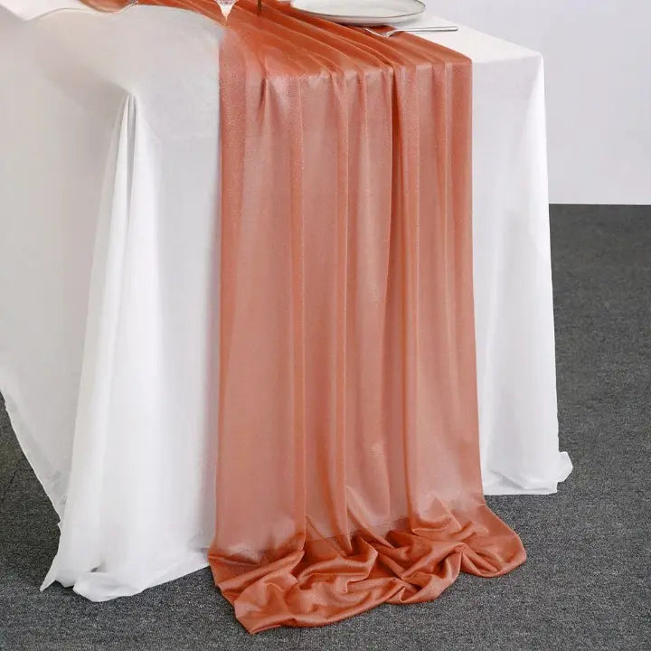 Chemin de table en organza couleur terracotta posé sur une table blanche pour décoration élégante