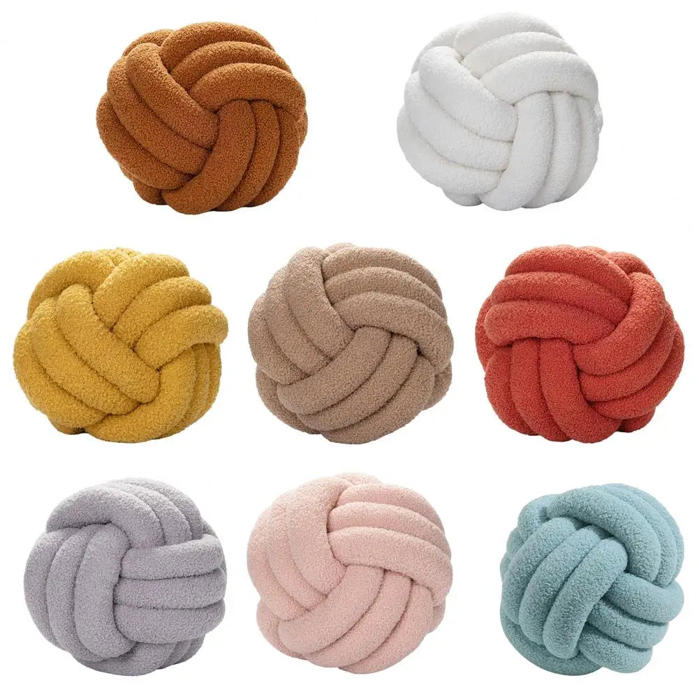 Coussin décoratif en forme de noeud présenté en différentes couleurs sur fond blanc