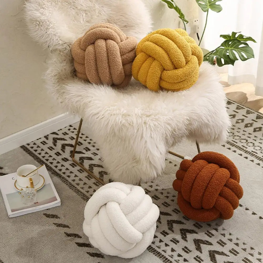 Coussins boule nouée en tissu bouclette disposés sur fauteuil et sol dans un salon moderne