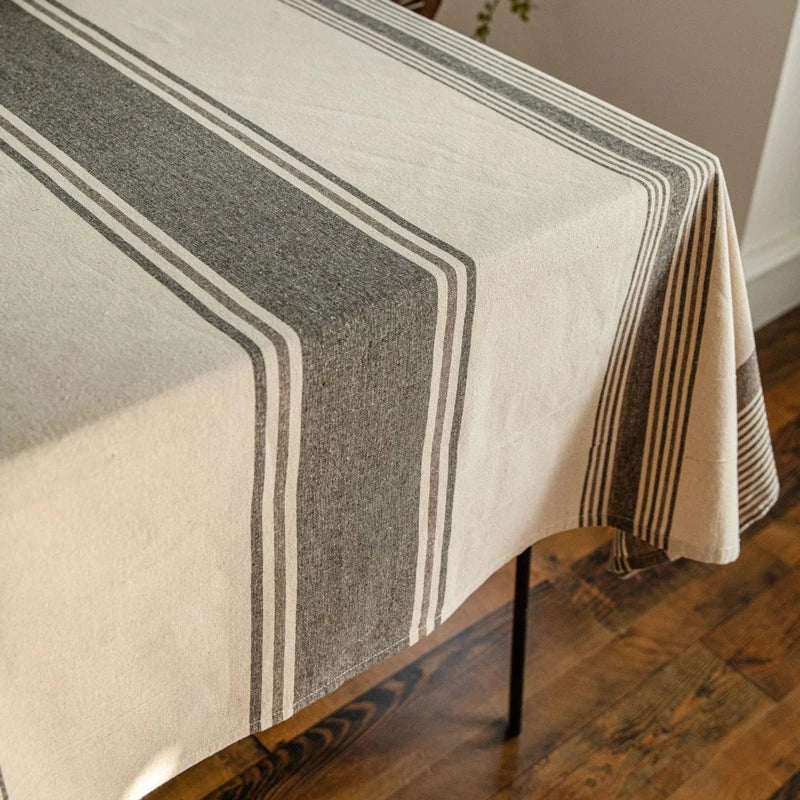 Détail de l’angle d’une nappe beige à rayures grises montrant la finition et le tombé du tissu