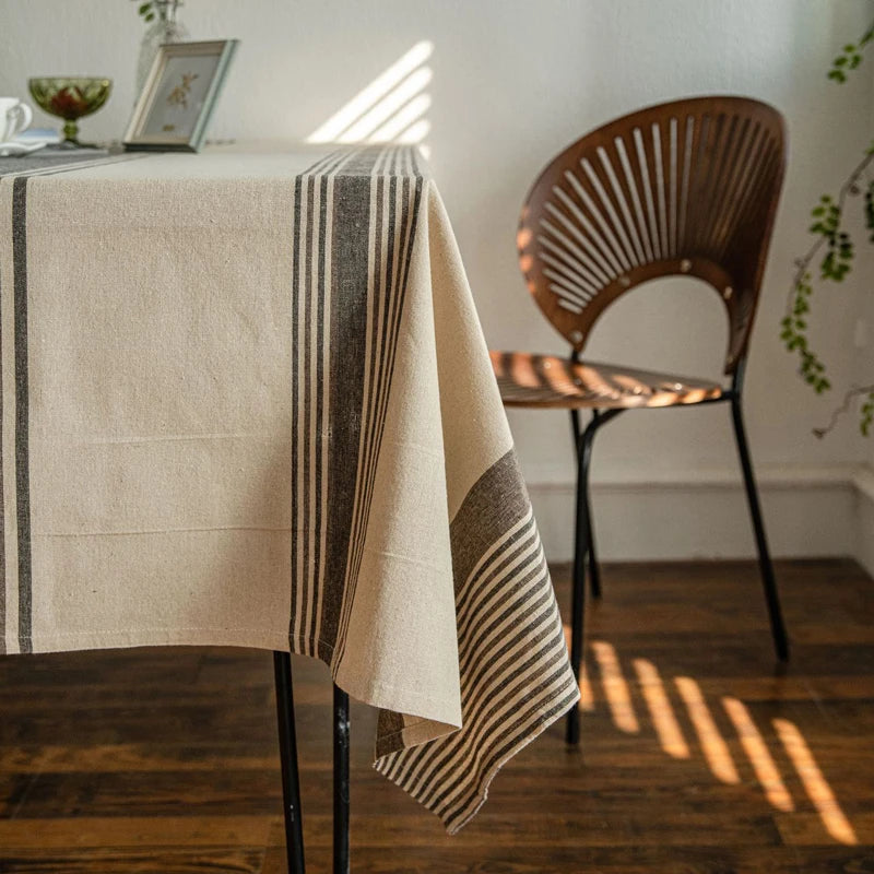 Nappe beige à rayures grises posée sur une table de salle à manger avec chaise en bois et lumière naturelle