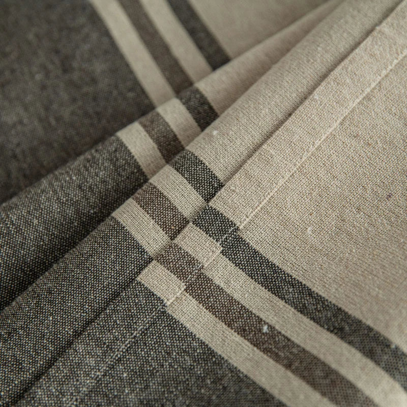 Gros plan du tissu d’une nappe en coton beige avec rayures gris foncé, texture naturelle et tissage visible